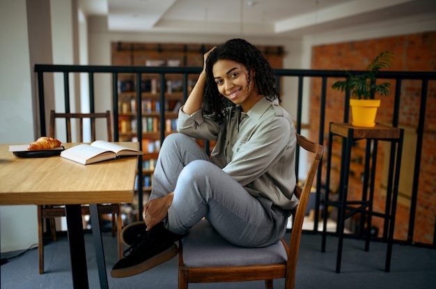 Allegro studentessa seduta al tavolo nella caffetteria della biblioteca. Donna che impara una materia, un'istruzione e una conoscenza. Ragazza che studia nella caffetteria del campus