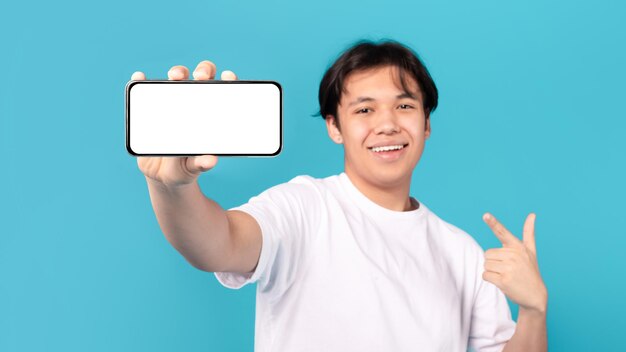 Allegro teenager asiatico che mostra lo schermo del telefono su sfondo blu Panorama