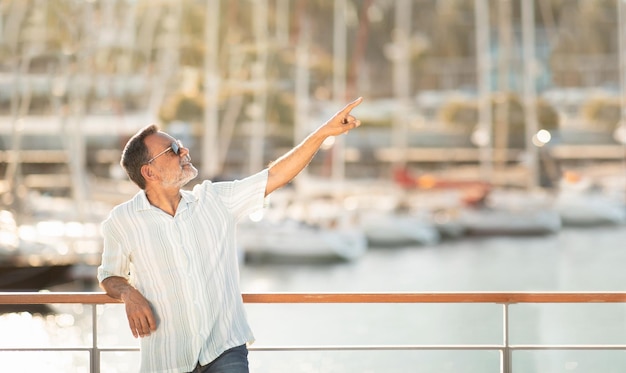 Allegro uomo anziano che punta il dito da parte in posa sullo sfondo del porto turistico