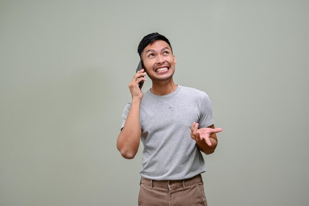 Allegro uomo asiatico che parla al telefono in piedi su uno sfondo verde studio