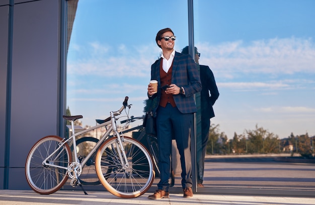 Allegro uomo d'affari con bicicletta e caffè da asporto