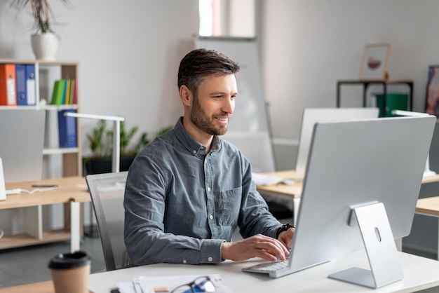 Allegro uomo d'affari di mezza età seduto al tavolo da lavoro digitando sulla tastiera del computer lavorando