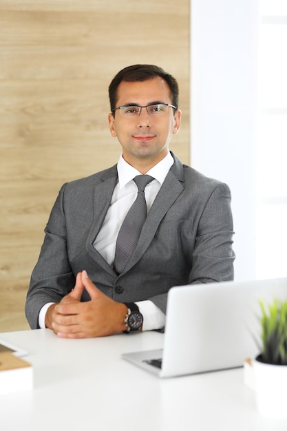 Allegro uomo d'affari sorridente seduto a una scrivania in un ufficio moderno Primo piano del volto di un imprenditore maschio o di un direttore aziendale sul posto di lavoro Concetto di business