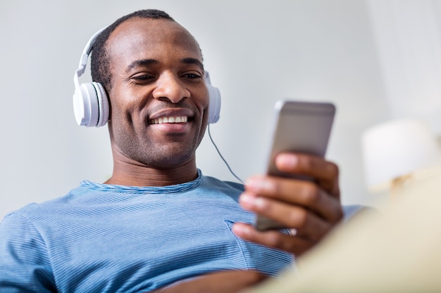 Allegro uomo gioioso felice sorridente e guardando lo schermo dello smartphone mentre si ascolta la sua canzone preferita