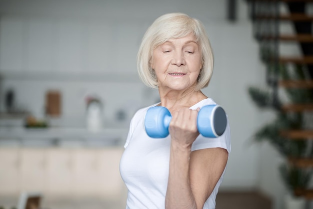 Allenamento a casa. Donna senior dai capelli corti che si esercita con i dumbbells