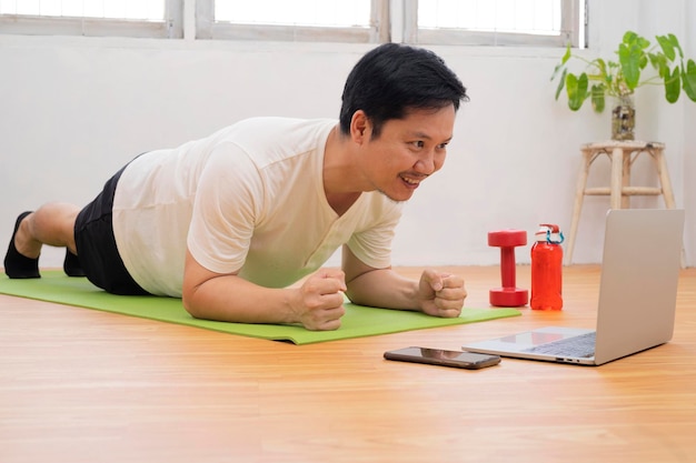 Allenamento a casa Uomo sportivo che fa yoga plank mentre guarda il tutorial online sul laptop