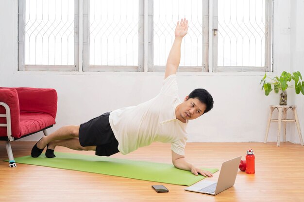 Allenamento a casa Uomo sportivo che fa yoga plank mentre guarda il tutorial online sul laptop