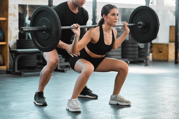 Allenamento bodybuilder donna attiva e sollevamento pesi con un personal trainer in palestra Giovane atleta in forma e atletica solleva un bilanciere con il suo allenatore in una palestra