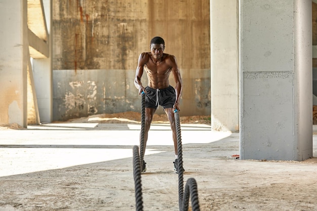 Allenamento con la corda Uomo sportivo che fa esercizio di corde da battaglia all'aperto Atleta maschio nero che si esercita facendo allenamento fitness funzionale con corda pesante