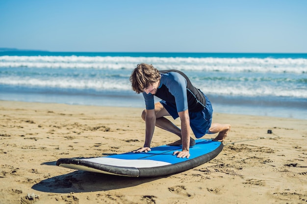 Allenamento del surfista del giovane prima di andare alla formazione su una spiaggia di sabbia. Imparare a navigare. Concetto di vacanza. Vacanze estive. Turismo, sport