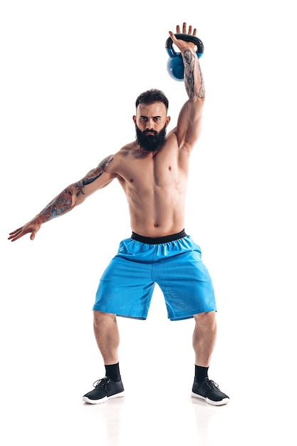 Allenamento di bodybuilder atleta maschio barbuto tatuato senza camicia muscolare con kettlebell