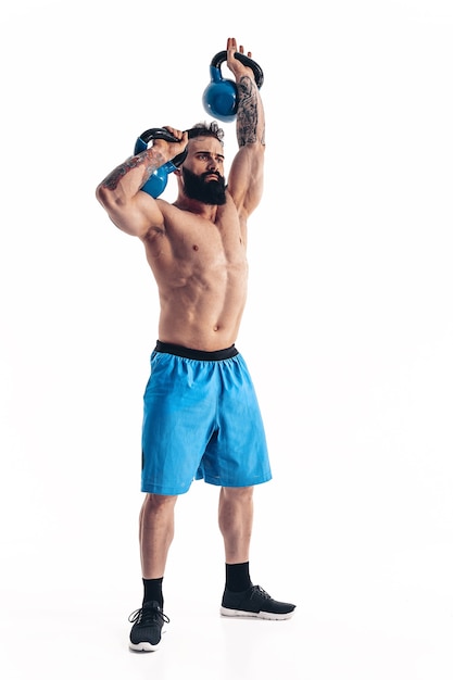 Allenamento di bodybuilder atleta maschio barbuto tatuato senza camicia muscolare con kettlebell
