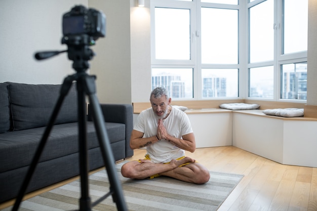 Allenamento in linea. Un uomo maturo in maglietta bianca che pratica yoga online