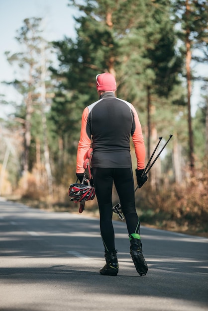 Allenare un atleta sui pattini a rotelle Giro di biathlon sugli skiroll con i bastoncini da sci nel casco Allenamento autunnale Sport sui pattini L'atleta va e tiene in mano l'attrezzatura sportiva