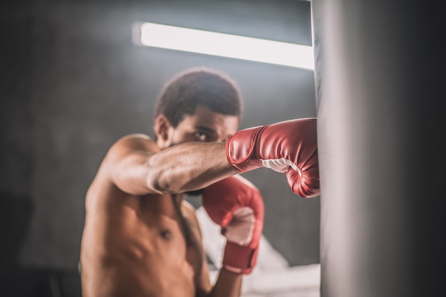 Allenarsi. Kickboxer dalla pelle scura che si allena in palestra e sembra coinvolto