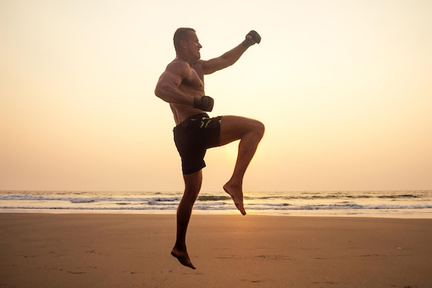 Allenatore a torso nudo forte pugile durante l'esercizio di kickboxing con allenatore in guantoni da boxe al tramonto. figura sportiva, motivazione perfetta dei muscoli addominali