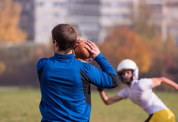 Allenatore della squadra che lancia la palla nel gruppo di giovani giocatori di football americano in azione durante l'allenamento sul campo