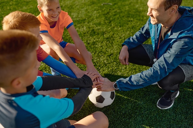 Allenatore di calcio che motiva la squadra di calcio junior prima della partita che impila insieme le mani sulla palla