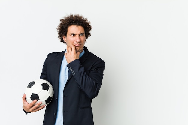 Allenatore di calcio in possesso di una palla rilassata pensando a qualcosa guardando uno spazio di copia.