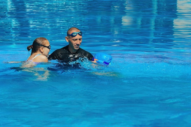 Allenatore di nuoto che dà lezione con due ragazze nella piscina all'aperto con acqua blu in una calda giornata di sole