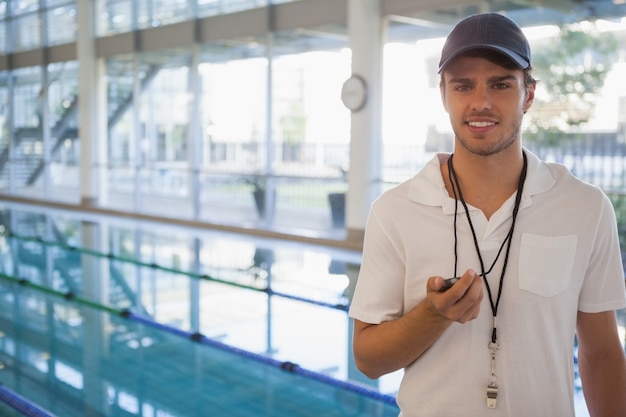 Allenatore di nuoto in piedi accanto alla piscina sorridendo alla telecamera