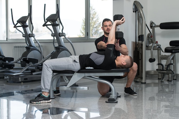 Allenatore di palestra che aiuta l'uomo sull'esercizio del torace