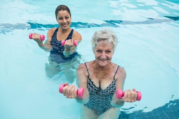 Allenatore femminile e donna senior che si esercita con i dumbbells in piscina