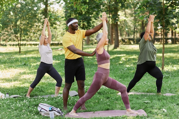 Allenatore sportivo che assiste un gruppo di donne anziane che si godono lo yoga all'aperto nel parco