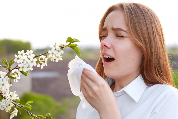 Allergia stagionale Piuttosto giovane femmina soffia il naso e starnutisce