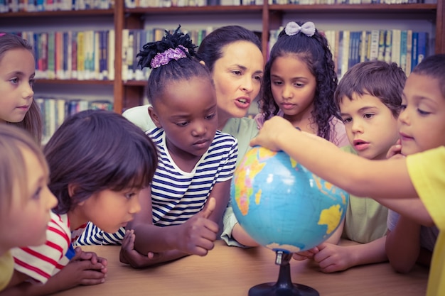 Allievi ed insegnante che esaminano globo in biblioteca