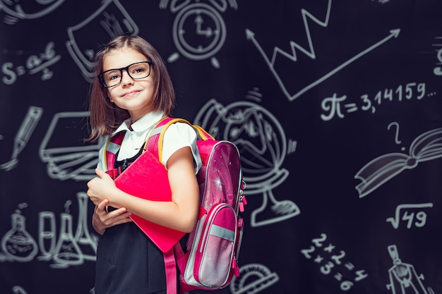 Allievo carino con gli occhiali che si prepara per andare a scuola con lo zaino e il libro in mano per tornare a scuola