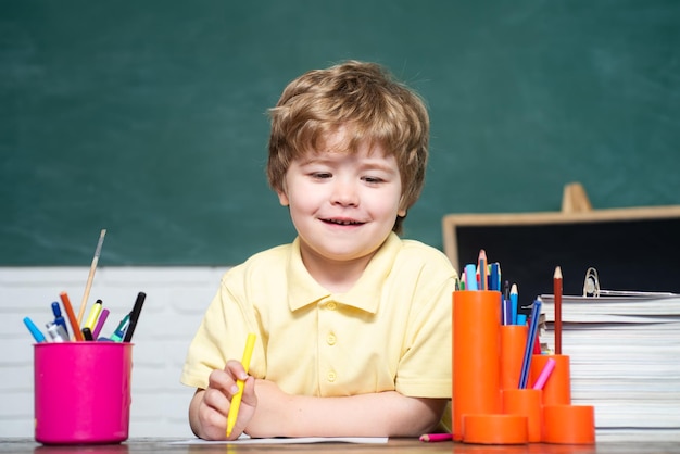 Allievo del ragazzino con l'espressione del viso felice vicino alla scrivania con il concetto di scuola di forniture scolastiche litt divertente
