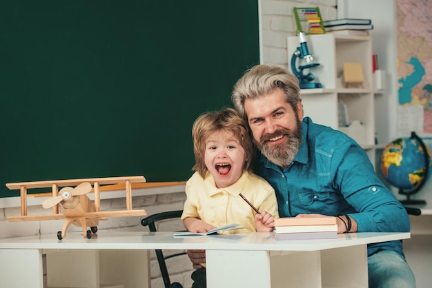 Allievo del ragazzino con l'espressione del viso felice vicino alla scrivania con materiale scolastico dopo l'insegnamento scolastico ele