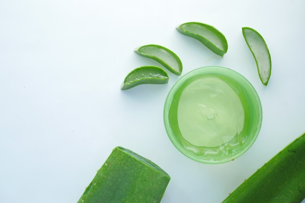 Aloe vera fresca a fette e gel liquido in un contenitore di plastica su sfondo bianco