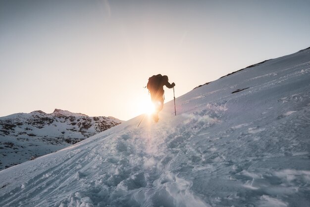 Alpinista che scala sulla montagna innevata nel tramonto splendente