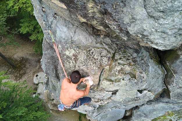 Alpinista determinato che si arrampica su una parete ripida di una montagna rocciosa Sportivo che supera percorsi difficili Partecipazione a sport estremi e concetto di hobby di arrampicata su roccia