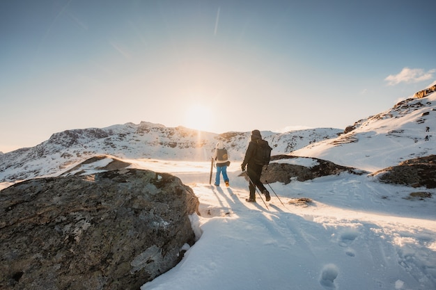 Alpinista due che fa un'escursione per picco montagna sul campo di neve al tramonto