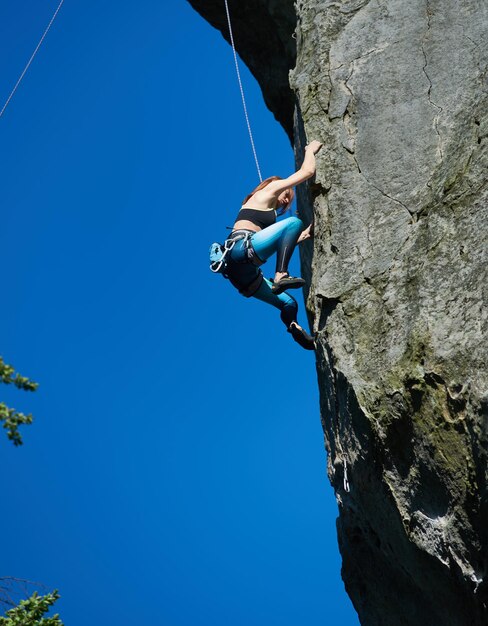 Alpinista femminile che scala la montagna sotto il cielo blu