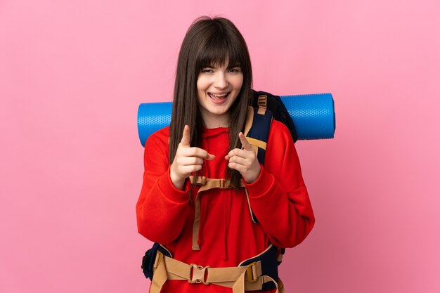 Alpinista ragazza ucraina con un grande zaino isolato sul muro rosa punta il dito contro di te