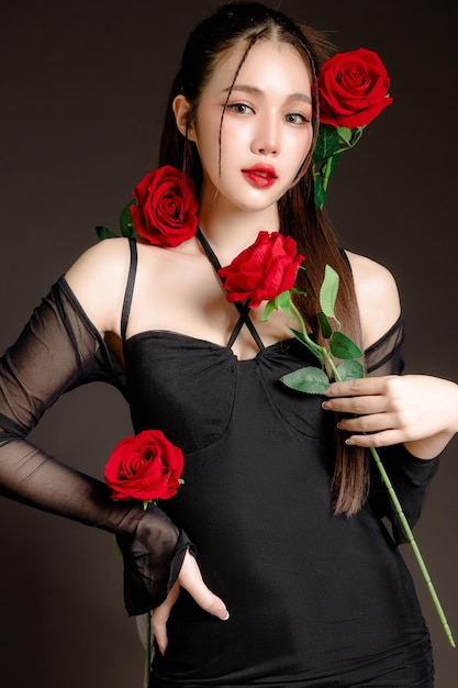 Alta moda di perfetto corpo slim fit bel viso giovane donna asiatica elegante in abito nero sexy con rose rosse su sfondo grigio scuro isolato Chirurgia plastica e cosmetologia
