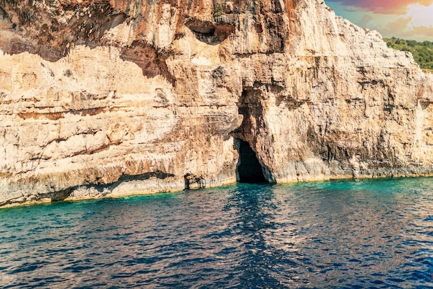 Alta scogliera lapidata sulla spiaggia del mare dell'isola di Corfù al tramonto