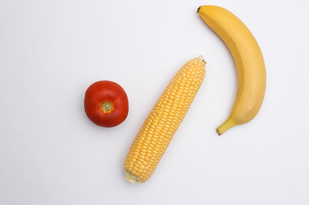 Altalena di mais, pomodoro e banana su sfondo bianco.