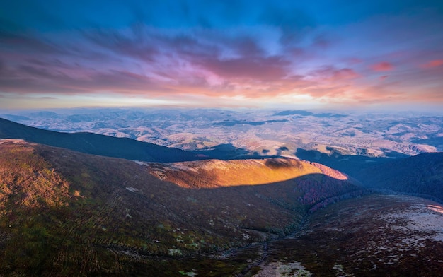 Alte cime montuose ricoperte di erba e un sottile strato di neve e ombre di nuvole sotto il cielo con soffici nuvole galleggianti rosa al tramonto