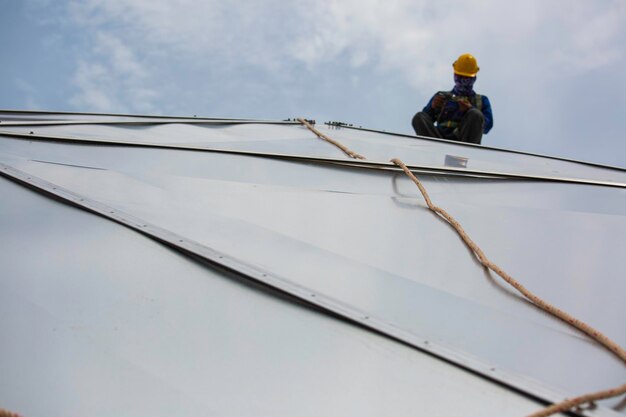 Altezza di accesso della fune dei lavoratori di sesso maschile che si collega con la cupola del serbatoio dell'olio da cantiere con imbracatura di sicurezza a otto nodi