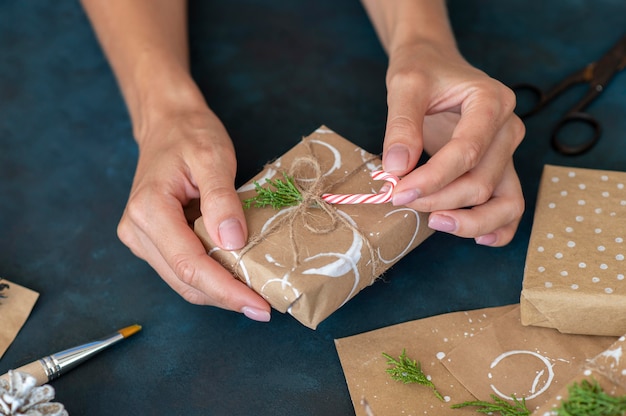 Alto angolo delle mani che decorano il regalo di Natale con il bastoncino di zucchero