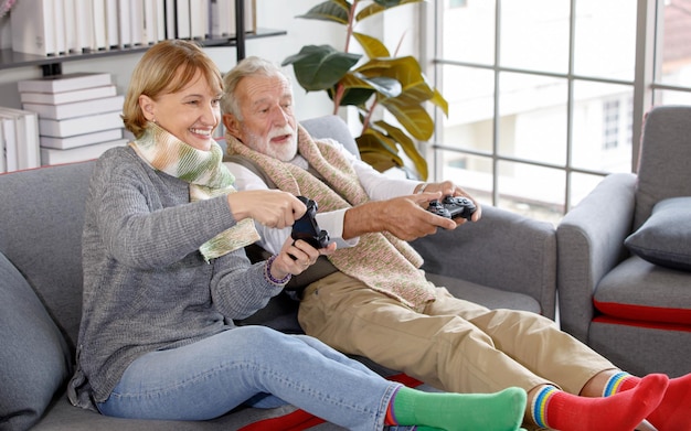Alto angolo di felice donna matura che usa il controller per giocare al videogioco con il marito anziano mentre è seduto sul divano insieme nel giorno del fine settimana a casa
