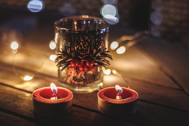 Alto angolo di piccole candele rosse che bruciano vicino al vetro con decorazioni natalizie sul tavolo durante la notte buia