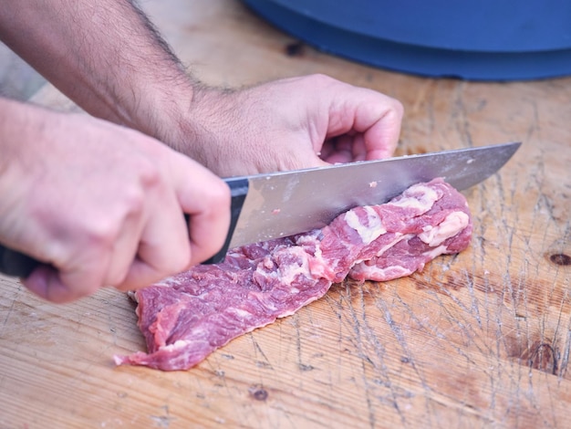 Alto angolo di raccolto macellaio maschio anonimo che taglia carne di maiale cruda con coltello affilato su tavolo di legno alla luce del giorno