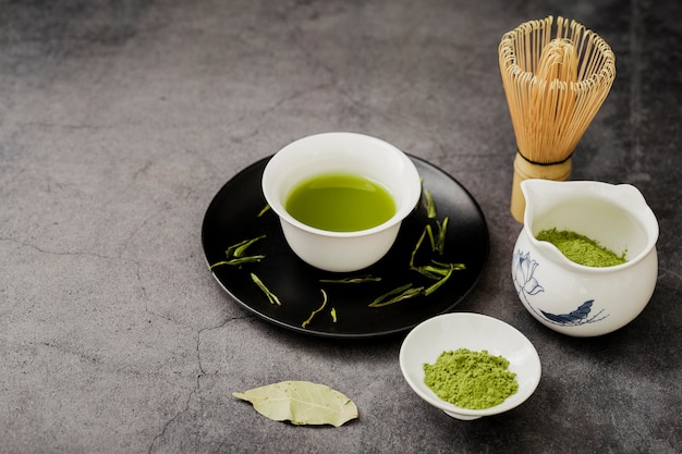 Alto angolo di tè matcha in tazza con piatto e foglia