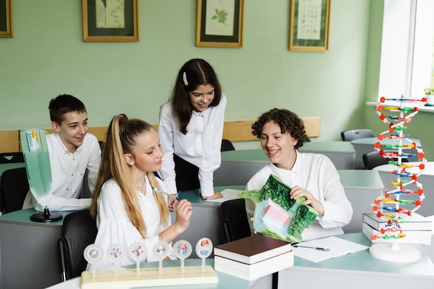 Alunni che comunicano e discutono in gruppo durante la lezione di biologia a scuola con DNA e modelli di cellule animali sul tavolo Istruzione a scuola di biologia e chimica